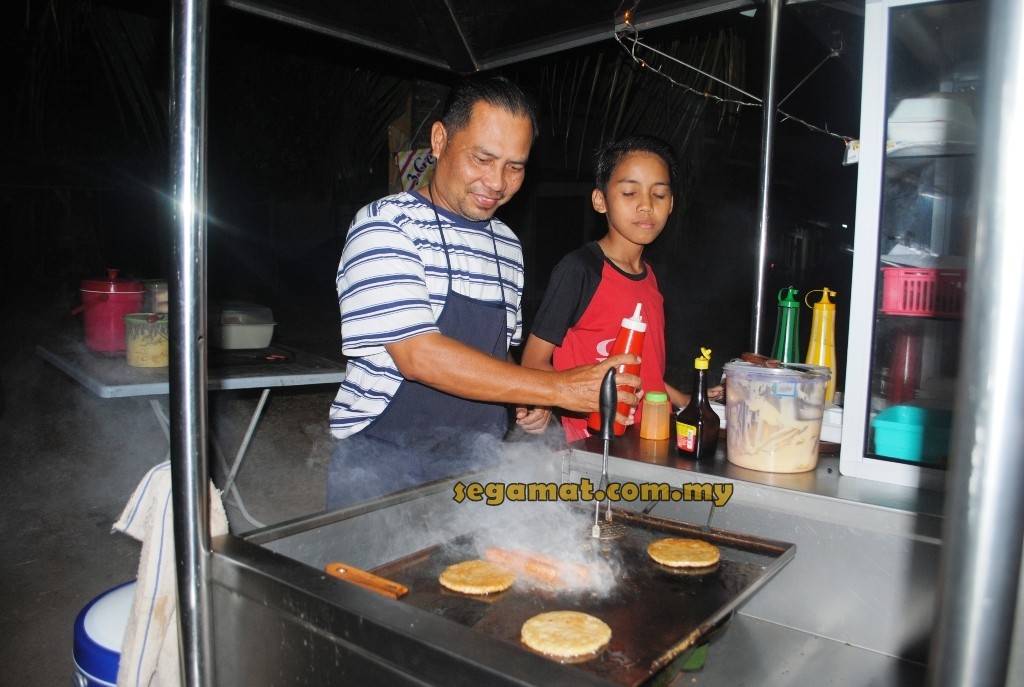 Rozi (kiri) sedang menyiapkan burger kukus untuk pelanggannya
