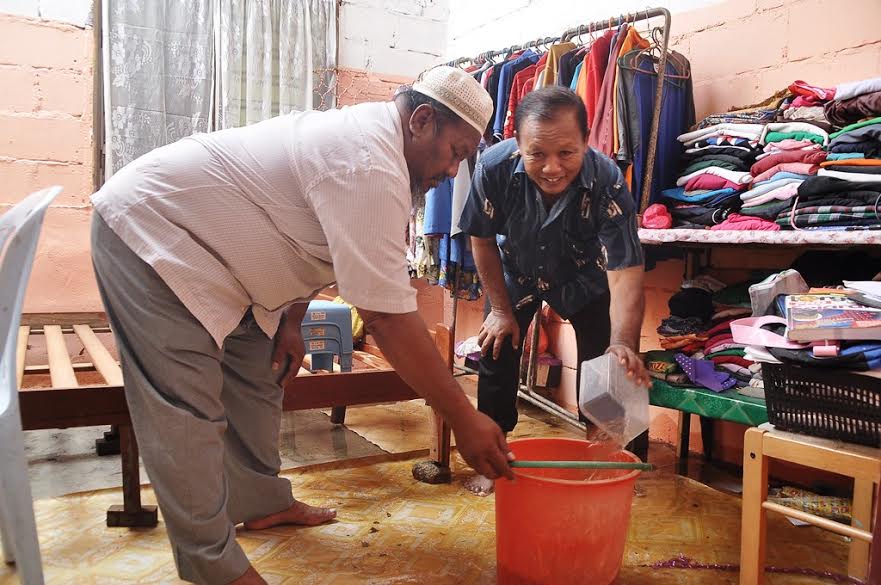 Mohd Hashim (kanan) menceduk air yang terdapat di biliknya sambil dibantu oleh Sabtu
