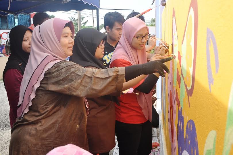 Haslinda (kiri) memberi tunjuk ajar kepada pelajar KKS yang membuat lukisan mural di dinding bangunan SK Kampung Tenang